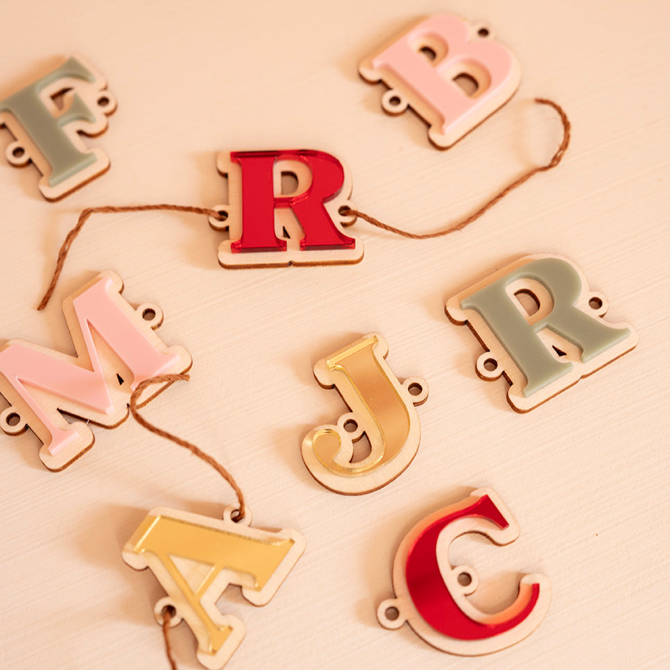Plusieurs lettres en bois et relief plexi coloré (alternance miroir or, rouge, rose et vert)
Il y a un trou de chaque côté la découpe du lettrage, une cordelette y est pasée