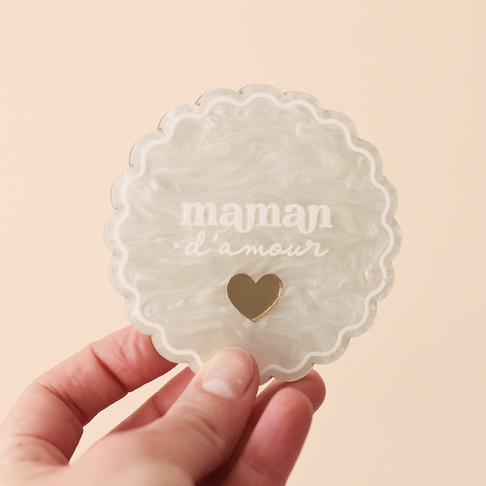 Miroir de poche forme rond festonné avec impression contour, inscription « maman d’amour » et coeur en plexi miroir incrusté au centre. Coloris face marbré blanc : fond plexi marbré blanc, contour et teste blanc, coeur en plexi miroir or