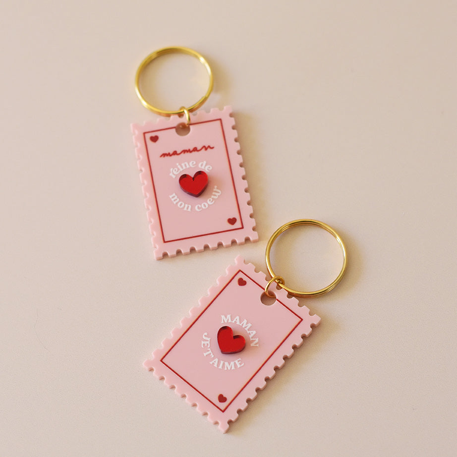 Porte-clés plexi coloré rose et rouge, design de carte à jour, forme de timbre et coeur au centre en relief, anneau doré. Inscription maman je t’aime ou reine de mon coeur