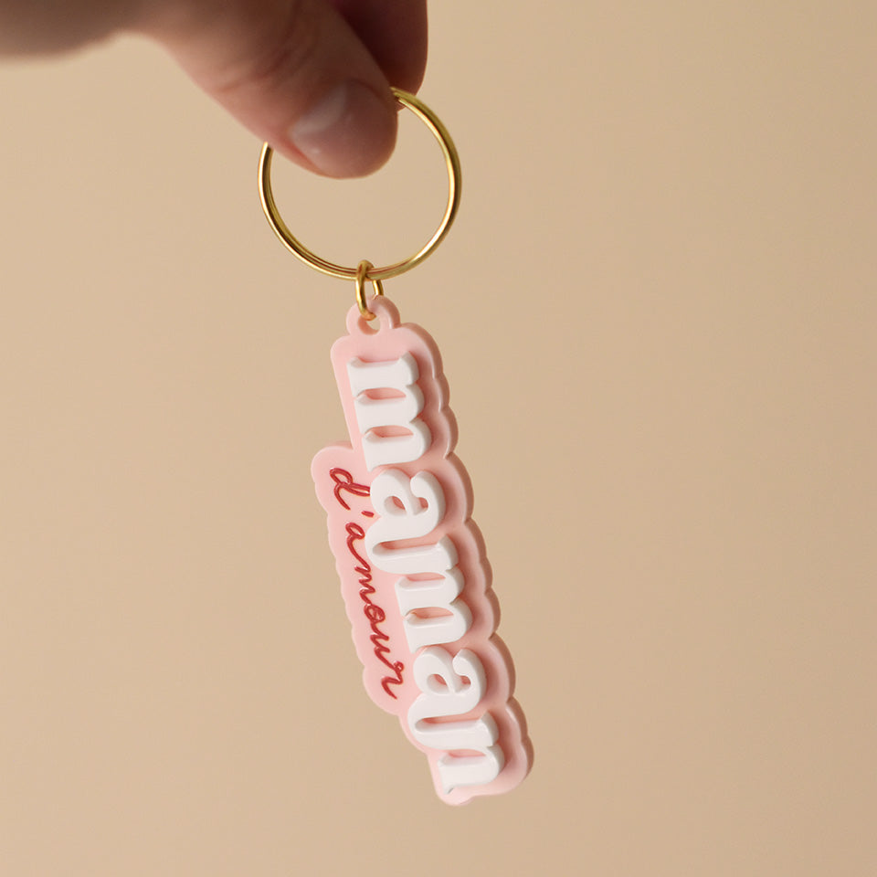 Porte-clés plexi coloré fond rose inscription « maman d’amour », « maman » en relief blanc et « d’amour » imprimé en rouge découpe à la forme du lettrage sur anneau doré