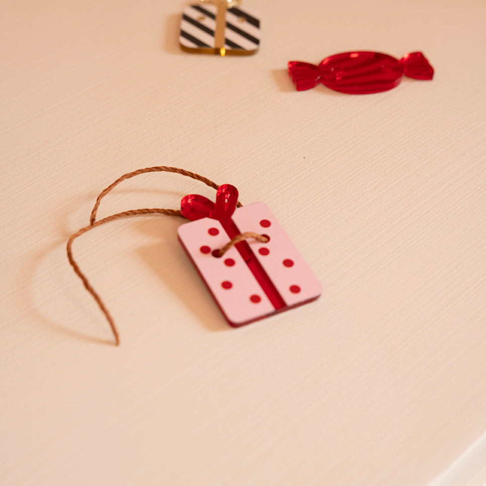 Découpes de plexi coloré avec impression de détails
Il y a 2 trous par découpes et une cordelette est passée dedans
Illustration d’un cadeau rose à pois et noeud rouges
 