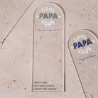 Marque-pages en plexi transparent découpe forme arche, texte blanc et coloré. Un modèle texte vert et blanc et un modèle texte bleu et blanc sont présentés.
Inscription dans l’arche sur 3 lignes « Cool Papa Club », 2 smiley entourent le mot « PAPA ».
En dessous est inscrit un prénoms (personnalisation du produit) 
En bas du marque-page est inscrit « Parque les papas cools lisent des livres » disposé sur 3 lignes avec un dessin de main en « v » 