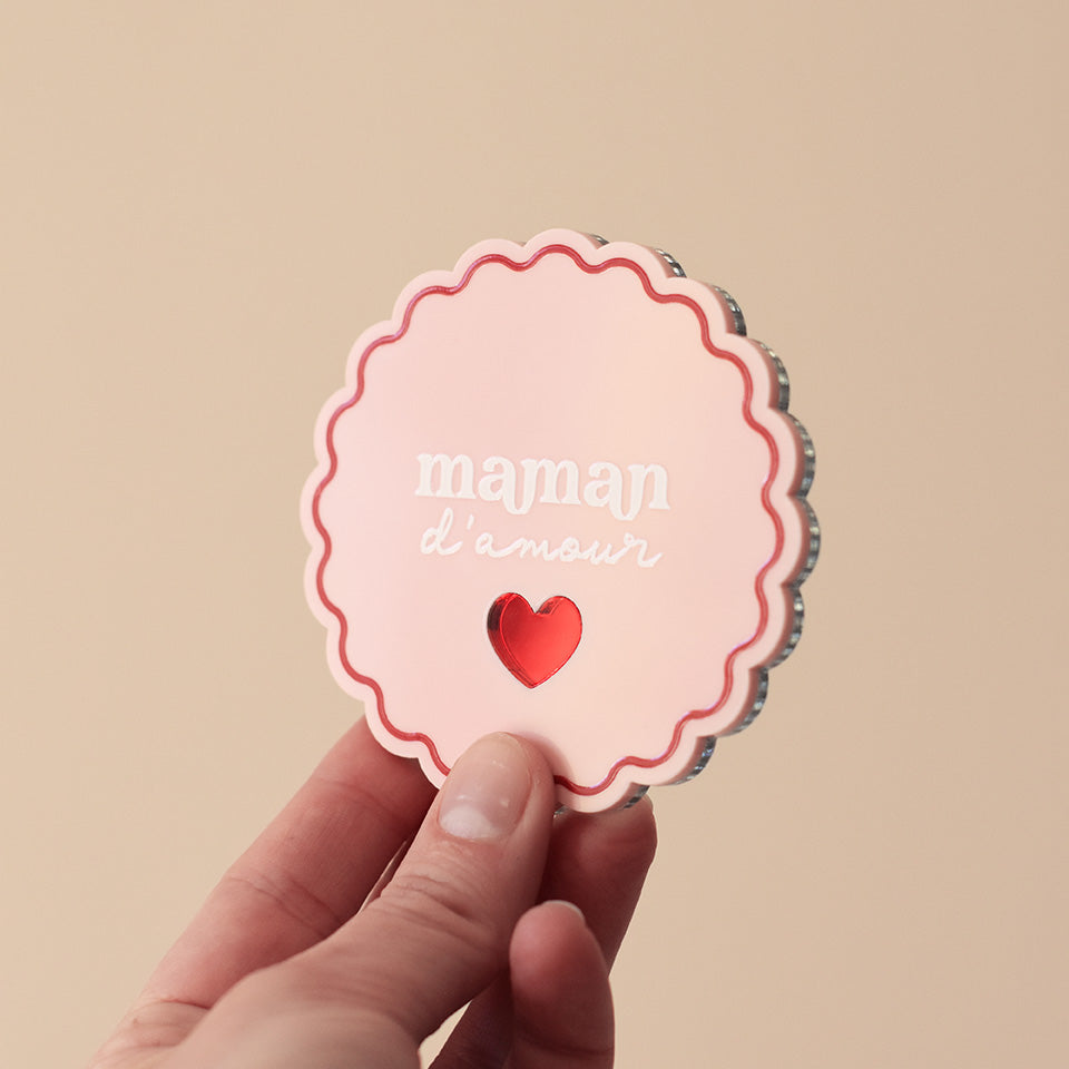Miroir de poche forme rond festonné avec impression contour, inscription « maman d’amour » et coeur en plexi miroir incrusté au centre. Coloris face rose et rouge : fond plexi rose, contour rouge, texte blanc, coeur en plexi miroir rouge