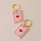 Porte-clés plexi coloré rose et rouge, design de carte à jour, forme de timbre et coeur au centre en relief, anneau doré.  Inscription maman je t’aime ou reine de mon coeur 
