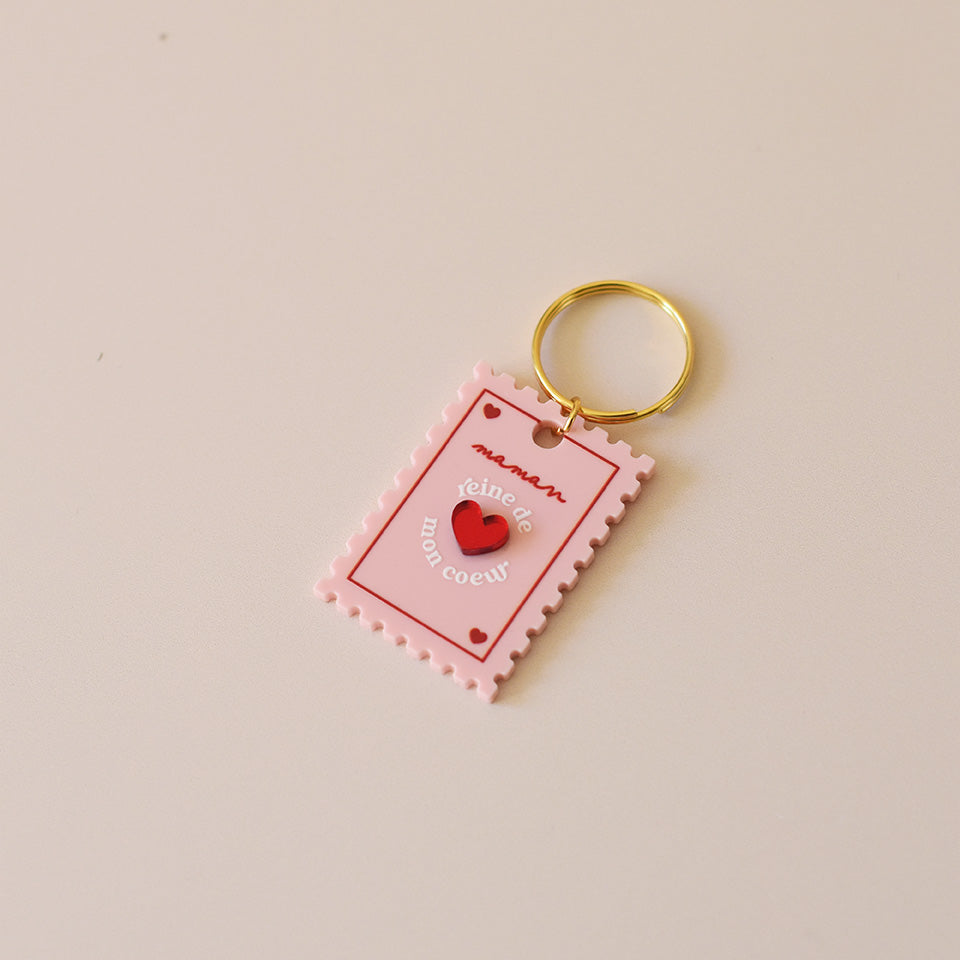 Porte-clés plexi coloré rose et rouge, design de carte à jour, forme de timbre et coeur au centre en relief, anneau doré.  Inscription reine de mon coeur 