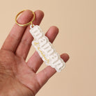 Porte-clés plexi coloré fond marbré blanc inscription « maman d’amour », « maman » en relief blanc et « d’amour » imprimé en doré, découpe à la forme du lettrage sur anneau doré